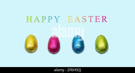 Frohe Osterkarte mit eingewickelten Schokoladeneiern auf blauem Hintergrund. Minimalistisches Design. Stockfoto