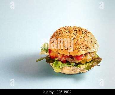 Frischer Rindfleisch-Burger mit Gemüse, Käse und Saucen auf hellblauem Papierhintergrund. Stockfoto