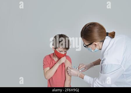 Ein Kind in einer medizinischen Maske wird gegen das Coronavirus in der covid Pandemie geimpft. Arzt in medizinischen Handschuhen mit einer Spritze macht eine Injektion. Cop Stockfoto