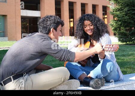 Ein junger lateinmann lehrt einer jungen lateinerin auf dem Universitätscampus, wie man Gitarre spielt. Universitätsleben, tausendjährige Generation. Stockfoto