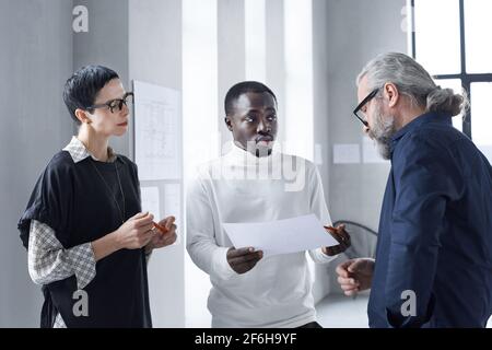 Junger afrikanischer Geschäftsmann diskutiert Dokument mit seinen erfahrenen Geschäftsleuten Während der Arbeit im Büro Stockfoto