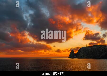 Ein goldener Sonnenuntergang mit der Silhouette eines felsigen Kaps über dem Meer. Sommer Meer Meer Strand Hintergrund. Niemand. Urlaub, Urlaub und Reisen Stockfoto