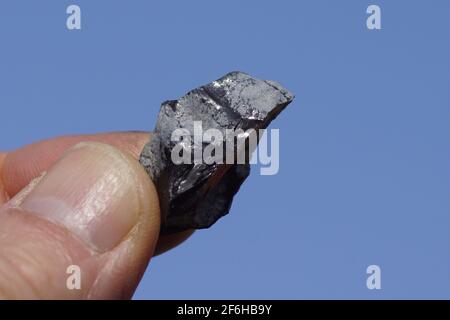 Hält ein Stück Obsidian in der Hand. Obsidianist ein natürlich vorkommendes vulkanisches Glas, das als extrausive, igneous Gestein gebildet wird. März, Niederlande. Stockfoto