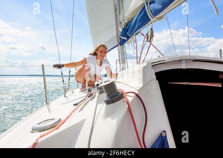 Junge Frau, die auf einer Yacht segelt. Weibliches Segelboot-Besatzungsmitglied trimmt Hauptsegel während der Segel im Urlaub in der Sommersaison Stockfoto