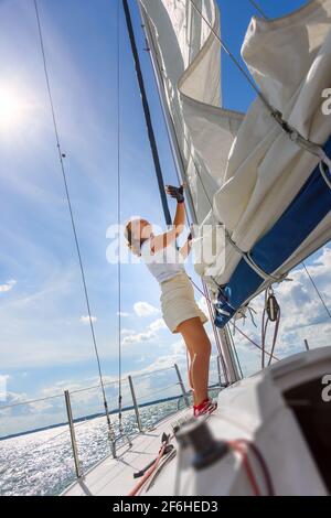 Junge Frau, die auf einer Yacht segelt. Weibliches Segelboot-Besatzungsmitglied trimmt Hauptsegel während der Segel im Urlaub in der Sommersaison Stockfoto