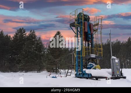 Ölpumpe unter dem Sonnenaufgangshimmel bei Sonnenuntergang. Ölpumpenheber Winter arbeiten. Oil Rig Energy Industriemaschine für Erdöl im Sonnenuntergang Hintergrund für desig Stockfoto