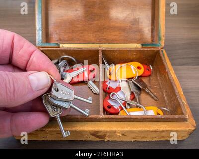 Nahaufnahme der Hand eines Mannes, der drei alte Schlüssel auf einem Ring von den vielen in einer schäbigen und abgenutzten alten lederbedeckten Holzkiste nahm. Stockfoto