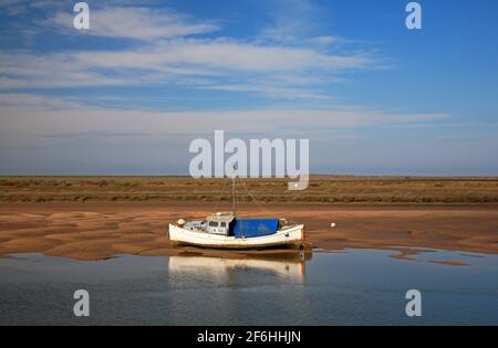 Ein Blick auf ein Küstenfischerboot mit Spiegelung, das auf flachen Gewässern in Overy Creek in Burnham Overy Staithe, Norfolk England, Großbritannien, aufgesetzt wurde. Stockfoto