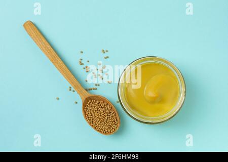 Glas mit Senf und Löffel mit Samen auf blauem Hintergrund Stockfoto