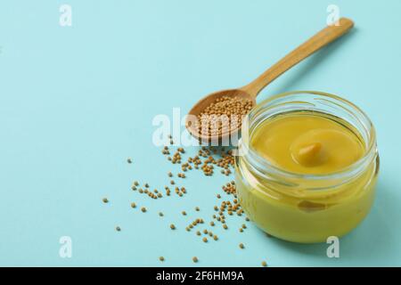 Glas mit Senf und Löffel mit Samen auf blauem Hintergrund Stockfoto