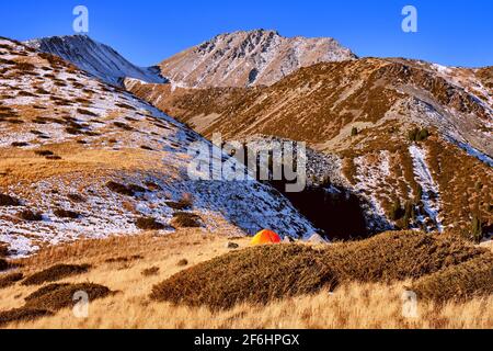 Zelt auf dem Bergrücken im Hochland auf dem Hintergrund des blauen Himmels, leuchtend orange Zelt flattert im Wind; Reise-und Tourismus-con Stockfoto