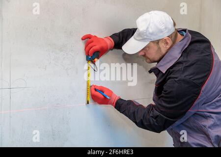 Ein Mann, ein Elektriker markiert mit Bleistift, Maßband und einer linearen Ebene zum Bohren von Löchern für Steckdosen Stockfoto