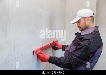 Ein Mann, ein Elektriker markiert mit Bleistift, Maßband und einer linearen Ebene zum Bohren von Löchern für Steckdosen Stockfoto