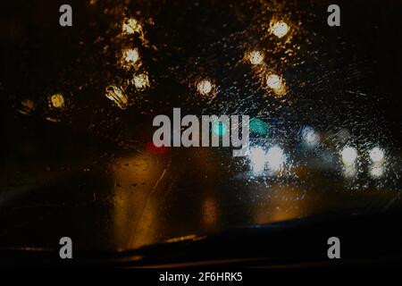 Regentropfen auf einer Windschutzscheibe mit einer Vielzahl von Lichtern und Reflektionen auf der Straße. Aufgenommen während der Überschwemmungen in Sydney im März 2021. Stockfoto