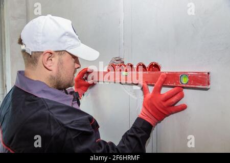 Ein Mann, ein Elektriker markiert mit Bleistift, Maßband und einer linearen Ebene zum Bohren von Löchern für Steckdosen Stockfoto