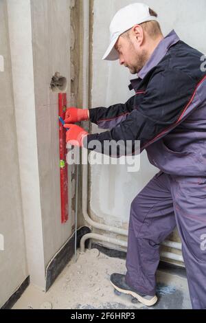 Ein Mann, ein Elektriker markiert mit Bleistift, Maßband und einer linearen Ebene zum Bohren von Löchern für Steckdosen Stockfoto