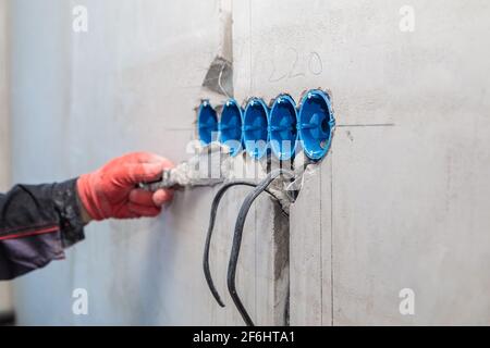 Der Elektriker putzt Löcher und Kanäle für Steckdosen und Drähte. Reparatur von Wohnungen. Nahaufnahme Stockfoto