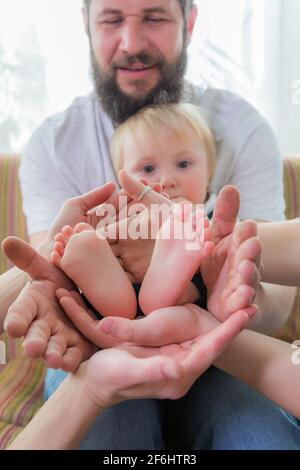 Die ganze Familie, Eltern und Kinder halten die Fersen des Babys in den Handflächen. Stockfoto