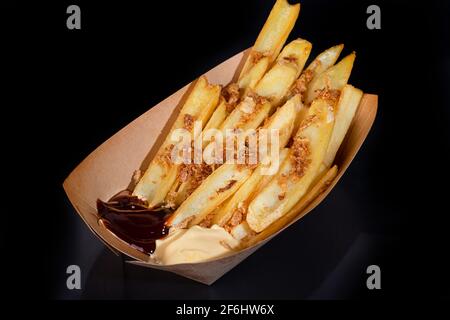Pommes frites mit zwei Saucen auf einem Pappteller. Essen zum Mitnehmen. Farbiger Hintergrund. Speicherplatz kopieren. Stockfoto