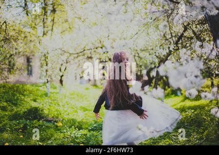 Kleines Mädchen in schwarzer Jacke und weißem Kleid tanzen in Der Kirschgarten im Frühling Stockfoto