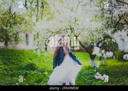 Kleines Mädchen in schwarzer Jacke und weißem Kleid tanzen in Der Kirschgarten im Frühling Stockfoto