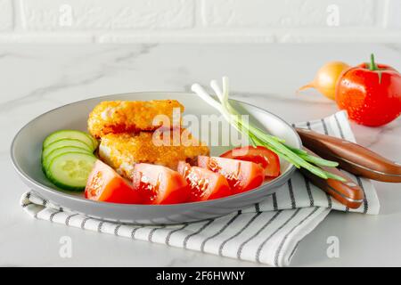 Gebratene panierte Fischfilets mit Gurkenamanttomaten, die aus nächster Nähe auf einem Teller serviert werden. Stockfoto