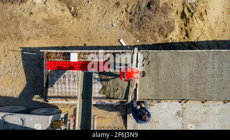 Oben Ansicht, Overhead auf Bauarbeiter Nivellieren frischen Beton mit Metallleiste in quadratischen Graben nach dem Gießen von Mischer LKW. Stockfoto