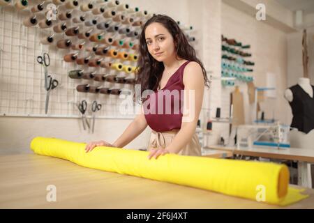 Cuaucasian weibliche Schneiderin nimmt Rolle von Stoff für Musterschnitt. Professioneller Modedesigner, der textiles Material misst. Bekleidungsindustrie Stockfoto