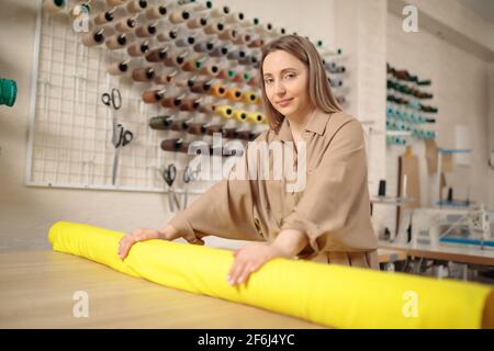Cuaucasian weibliche Schneiderin nimmt Rolle von Stoff für Musterschnitt. Professioneller Modedesigner, der textiles Material misst. Bekleidungsindustrie Stockfoto