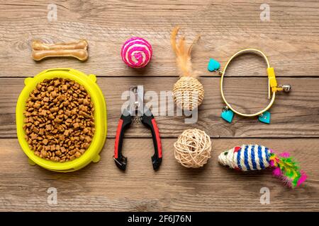 Trockenfutter in Schüssel, Spachtel, Nagelschere, Kragen, Maus, Kugeln, Knochen auf Holzhintergrund Draufsicht Flat Lay Spielzeug, Zubehör und Nahrung für Ihren belov Stockfoto