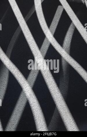 Abstraktes Design von Schatten und Licht durch geschwungene Öffnungen im Balkongeländer auf Betonboden strukturiertes welliges Design vertikaler Hintergrund Stockfoto
