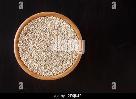 Getrocknete weiße Quinoa-Samen in Holzschüssel auf schwarzem Holz Hintergrund Stockfoto