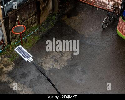 Regen fällt auf ein kleines Solarpanel hinter einer Straße Lampe in einer kleinen Gasse Stockfoto