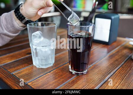 Ein Glas frische eiskalte Limonade auf einem Holztisch mit Kaffee. Nahaufnahme der männlichen Hand, Mann hält Eis Stockfoto