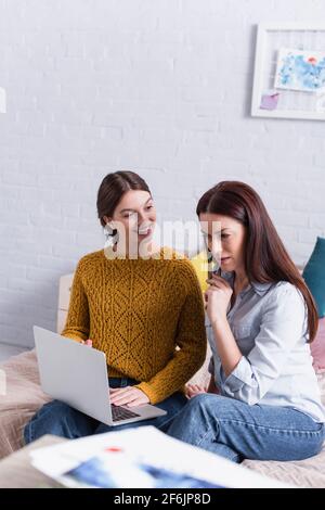 Lächelndes Teenager-Mädchen, das Mutter in der Nähe des Laptops im Schlafzimmer ansieht Stockfoto