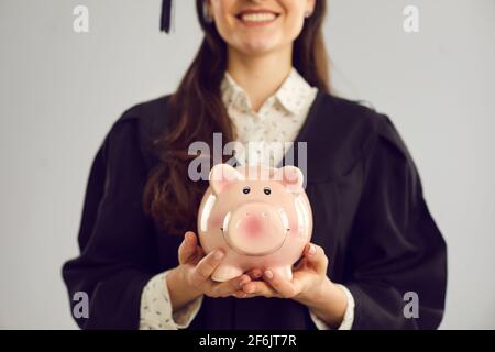 Zugeschnittenes Bild Nahaufnahme eines Sparschweines in den Händen einer Schülerin auf grauem Hintergrund. Stockfoto