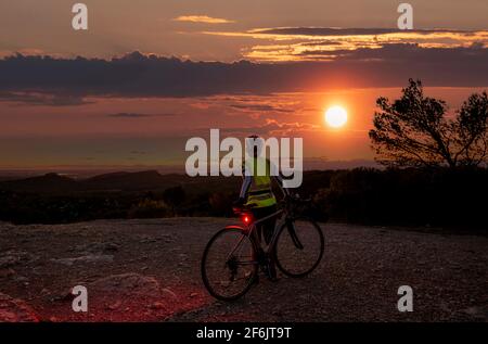 Reife weibliche Radfahrer bei Sonnenuntergang auf dem Gipfel des Alpilles, in der Nähe von San Remy, Provence, Frankreich. Stockfoto