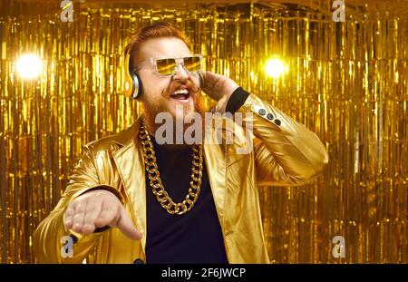 Fröhlicher DJ in glänzender Jacke, Kopfhörern und cooler Sonnenbrille, der Musik auf der Disco-Party spielt Stockfoto