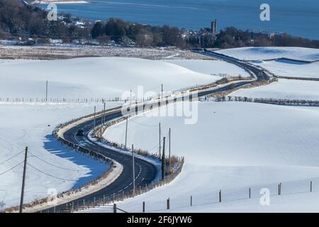 Verschneite Felder und eine Landstraße, die nach Burntisland, Fife, Schottland führt Stockfoto