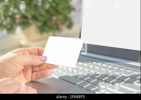 Online-Zahlung für Einkäufe per Mockup-Kreditkarte. Frau, die online mit Mockup-Laptop und Kreditkarte einkauft. Hände mit Plastikkreditkarte Stockfoto