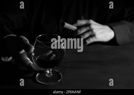 Mann Hände mit einem Glas Whiskey und eine Zigarre auf dunklen Tisch. Schwarz-weiß-Fotografie, Rauch und Alkohol sucht Konzept. Stockfoto