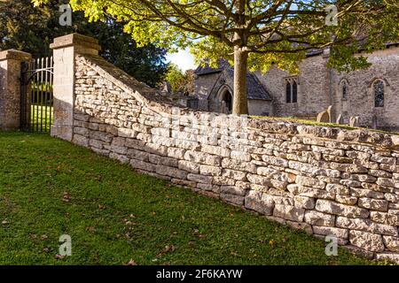 Abendlicht auf der Trockensteinmauer um die kleine normannische Kirche St. Michael im Cotswold-Dorf Winson, Gloucestershire, Großbritannien. Stockfoto