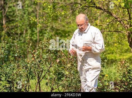 Älterer Mann in weißem Kleid mit Telefon in der Hand im Garten. Stockfoto