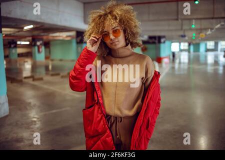 Serious Mixed Race Hip Hop Mädchen in Jacke in der Garage stehen und Anpassung Sonnenbrille. Stockfoto