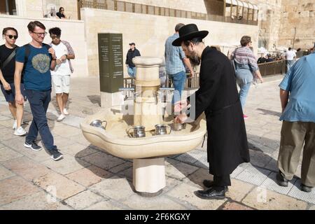 JERUSALEM, ISRAEL - 26. November 2019: Jüdischer orthodoxer Mann in einem schwarzen traditionellen Anzug und einem Hut, der sich mit einem traditionellen rituellen Becher die Hände wäscht Stockfoto