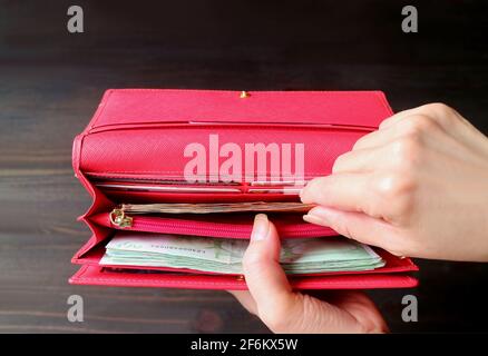 Die Hand der Frau hält einen Haufen Banknoten in einer roten Brieftasche Stockfoto