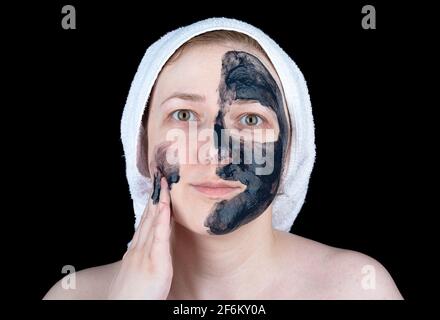 Eine junge Frau trägt eine kosmetische Peeling-Maske mit Aktivkohle auf ihr Gesicht auf. Gesichtspflege. Stockfoto