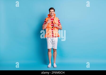 Ganzkörperfoto Mann trägt Rettungsweste auf dem Lächelnder Strand isoliert auf lebhaftem blauem Hintergrund Stockfoto