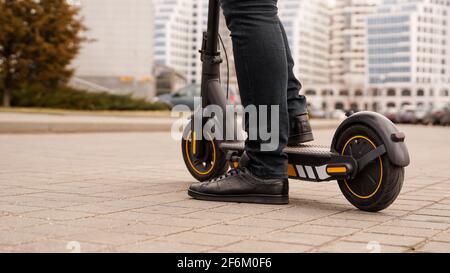 Zugeschnittenes Bild des jungen Mannes, der auf einem elektrischen Kickroller auf der Straße reitet Stockfoto