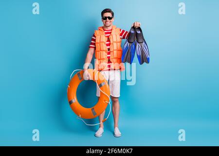 Ganzkörperfoto Mann trägt Rettungsweste Sonnenschutzscheibe halten flippers orange Kreis isoliert auf hellblauem Hintergrund Stockfoto